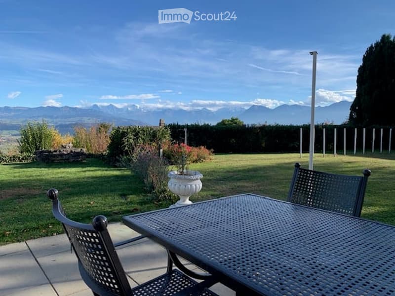 Outdoor patio with a metal table and chairs, overlooking a well-maintained lawn and distant mountain range.