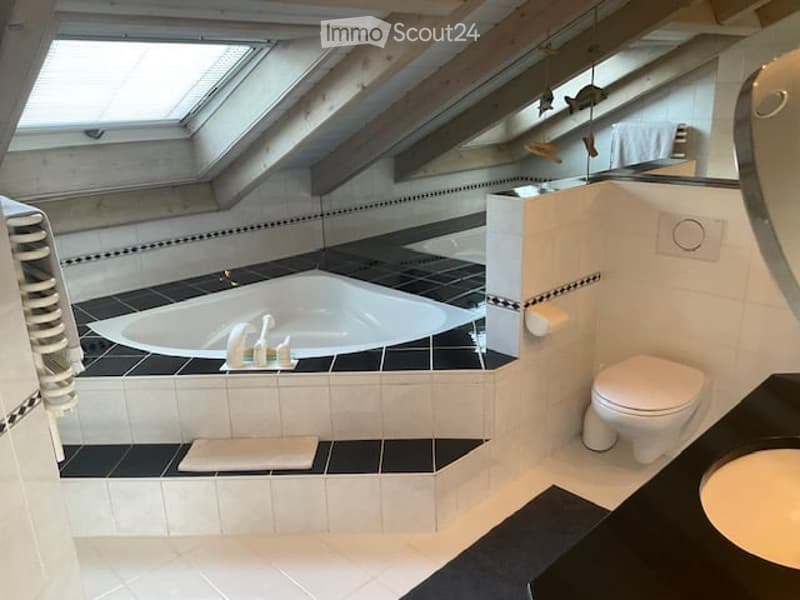 Modern bathroom with a large bathtub, toilet, sink, and mirror. The floor is tiled in black and white, and there is a towel on the edge of the bathtub.
