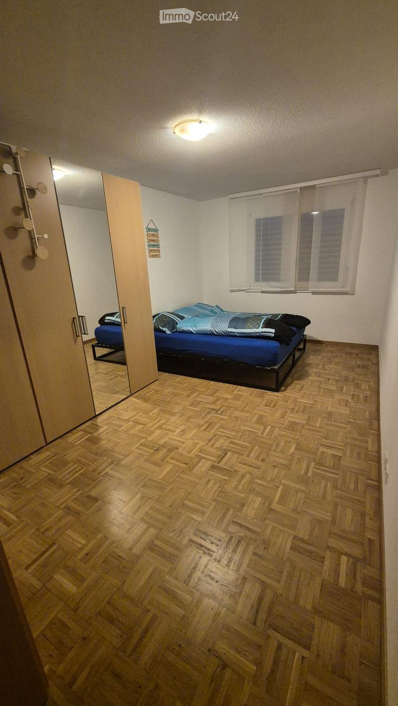 Cozy bedroom with wooden herringbone flooring, a single bed with blue bedding, a large mirror, and a wardrobe.