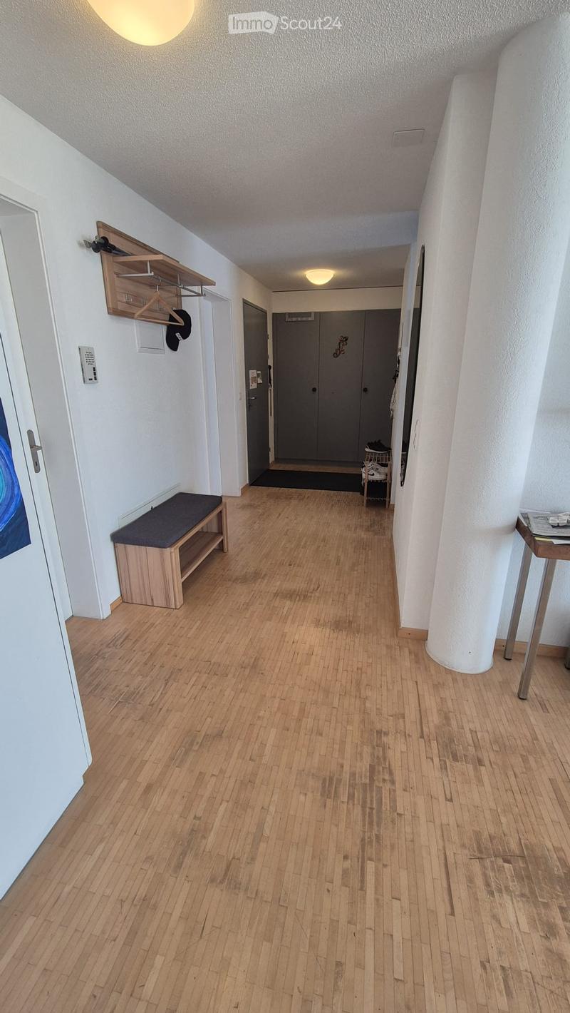 Clean hallway with wooden flooring, white walls, and a bench near the entrance. Features include a coat rack with hats, a small table, and a door leading to another room.