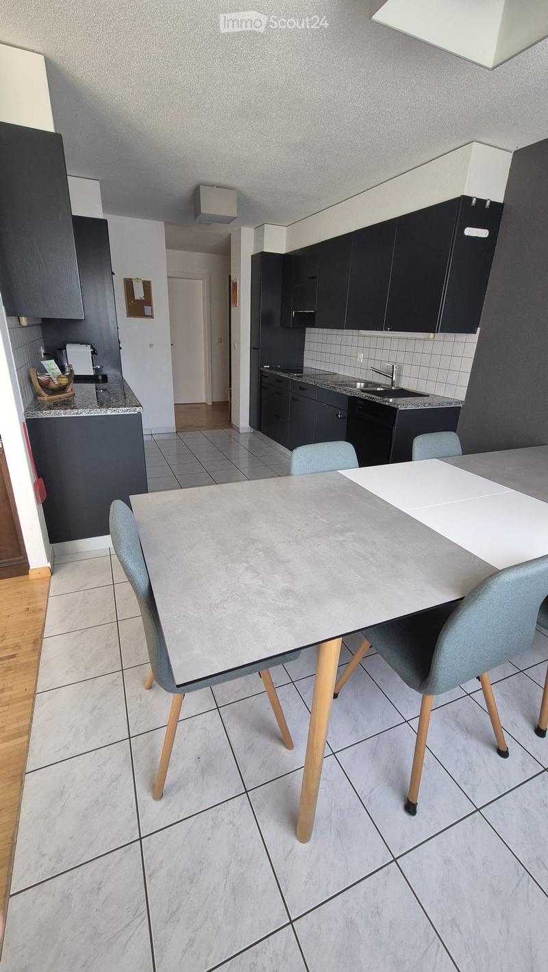 Modern kitchen with grey cabinets, marble countertops, and a dining area featuring a large table and four chairs.