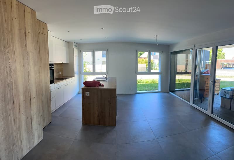 Modern kitchen with white cabinets, a wooden island, and large windows. The space includes a sink, faucet, and an oven, with a view of the garden through the sliding glass doors.