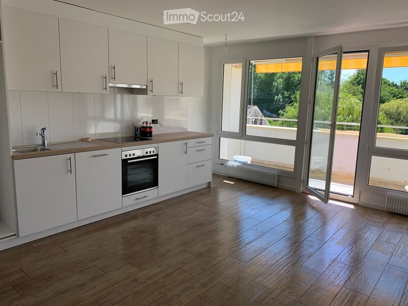 Modern kitchen with white cabinets, wooden countertops, and a stainless steel oven. Large windows with blinds offer a view of greenery outside.