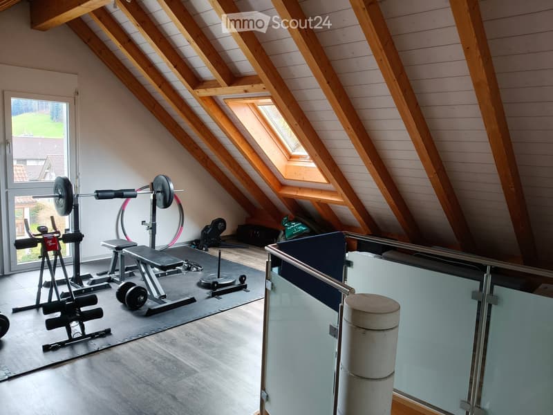 Attic room with wooden beams and skylights, equipped with a weight bench, dumbbells, and a fitness machine.