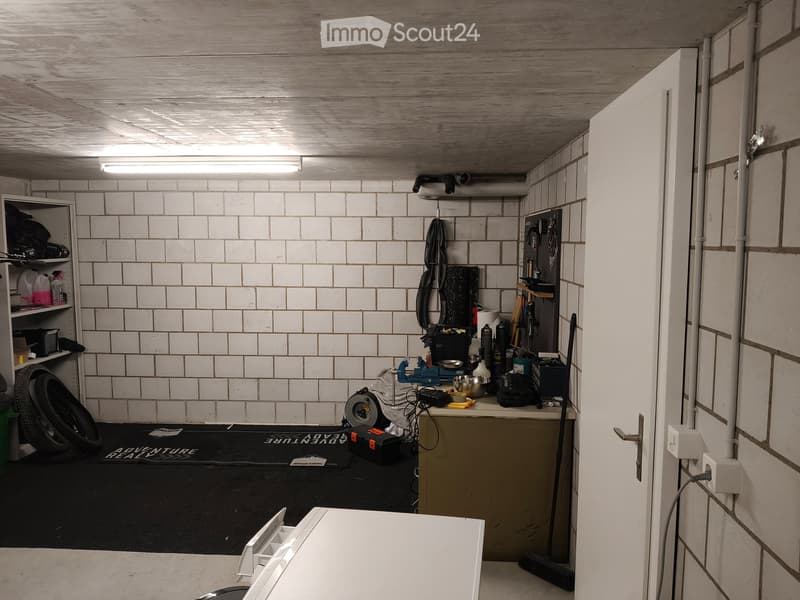 Garage with white brick walls, wooden ceiling, shelves, worktop, tools, tire, and a door.