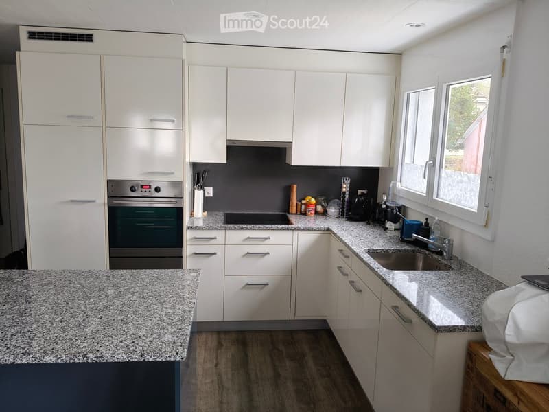 Modern kitchen with white cabinets, granite countertops, and stainless steel appliances including an oven and sink.