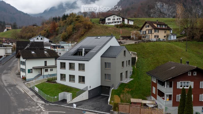 Modern architectural house on a hillside with solar panels, driveway, garden, and beautiful mountain views