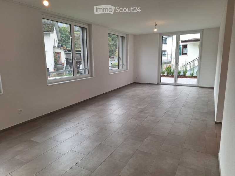 large room, light grey tiles, two large windows, glass door to a terrace