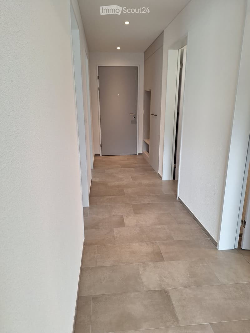 Long hallway, white walls, beige tiled floor, gray door