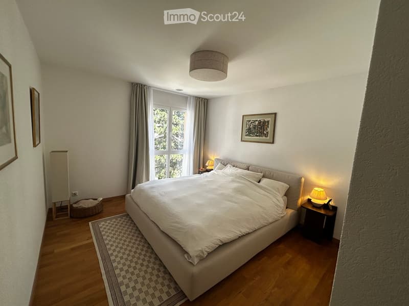Cozy bedroom with a large bed, nightstands, table lamps, framed artwork, and a dog bed near the window.