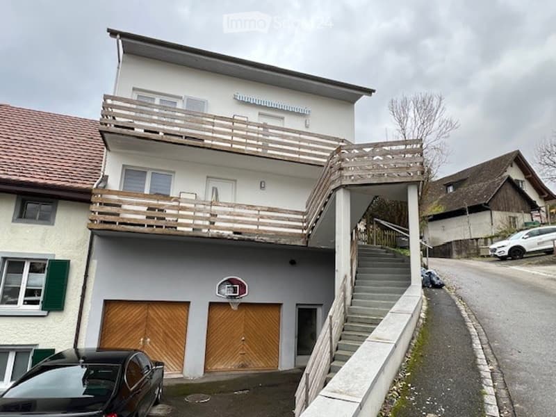 Two-story residential building with balconies, garage, and basketball hoop.