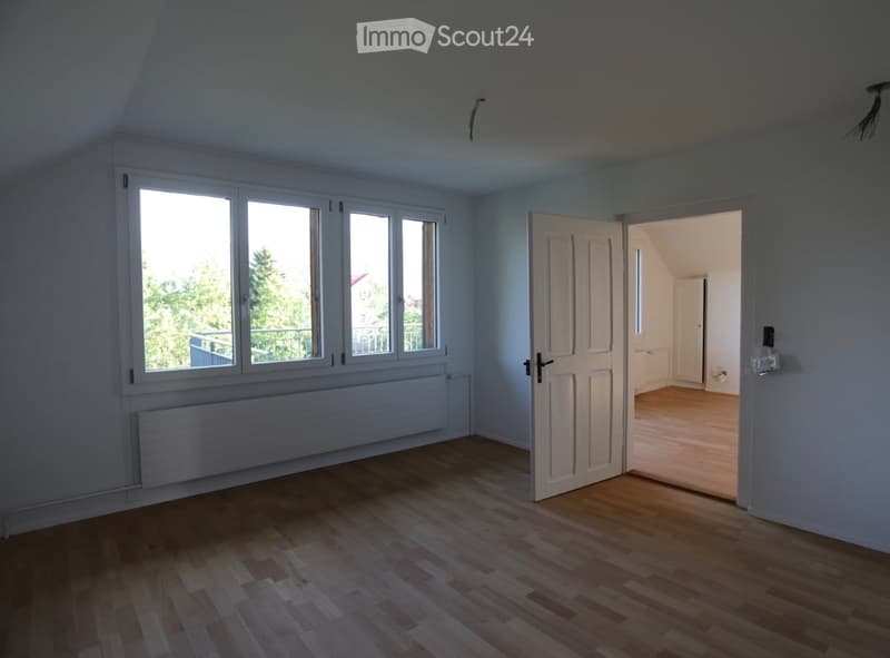 Empty room with wooden flooring, large windows, and an open door leading to another room.