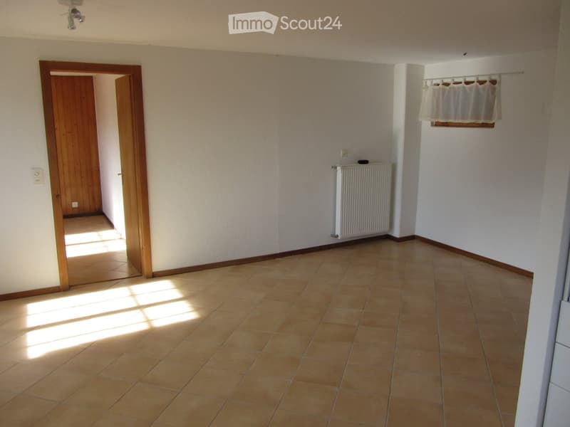 Empty room with tiled floor, white walls, wooden door, radiator, and window with curtain.