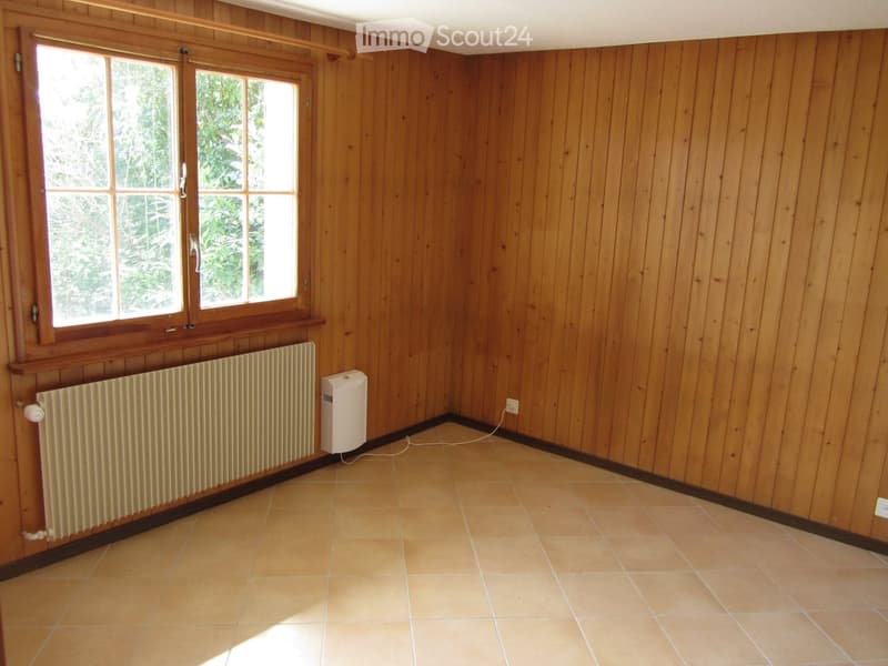 Empty room with wooden walls, tiled floor, large window, radiator, and small white appliance.