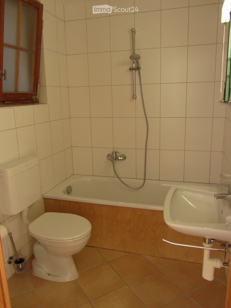 Bathroom with beige tiled walls, a white toilet, a bathtub with a handheld shower, and a sink with a faucet.