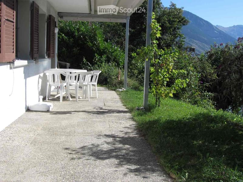 Outdoor patio area with a table and chairs, surrounded by greenery and a scenic mountain view in the background.