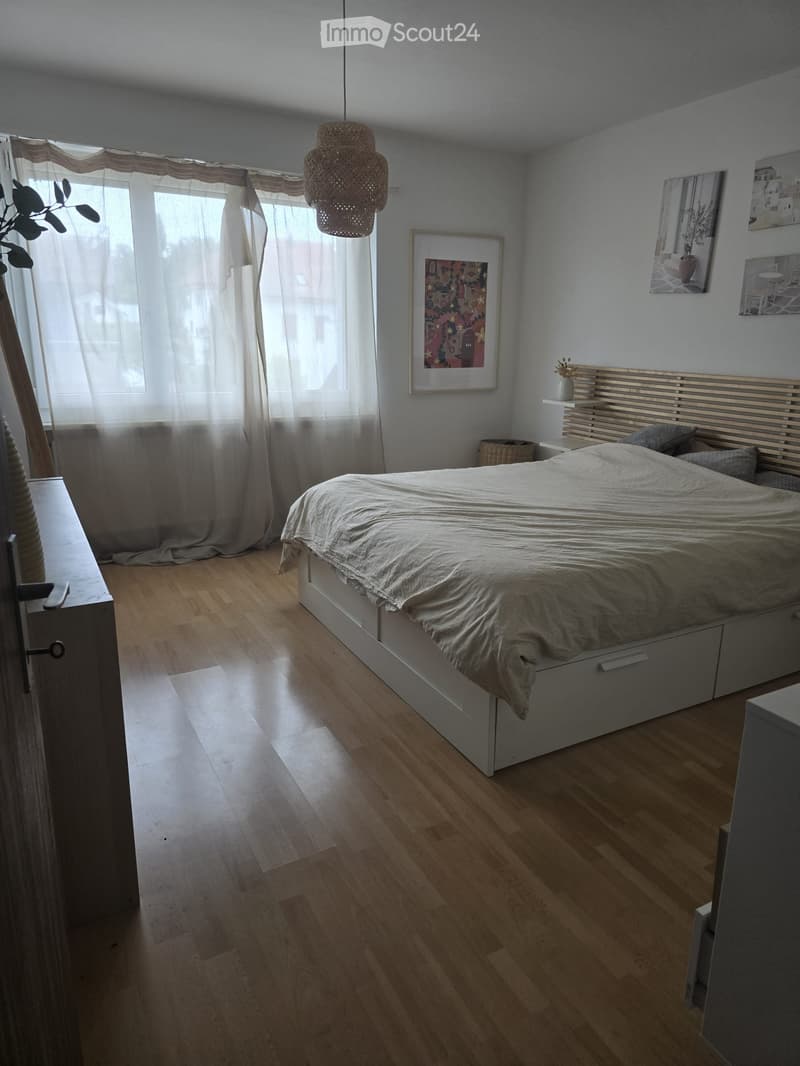 Modern bedroom with wooden flooring, a large bed with white bedding, a nightstand, and decorative artwork on the walls.