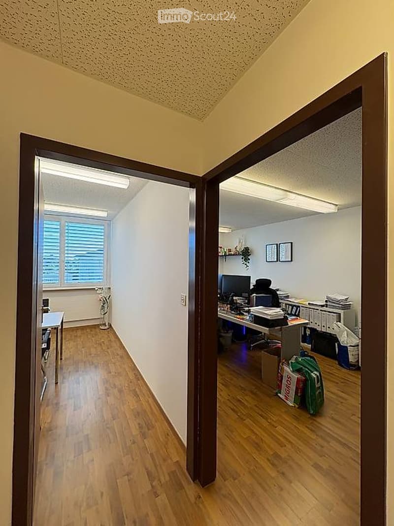 Two connected rooms with wooden flooring, desks, chairs, computers, filing cabinets, and decorative items.
