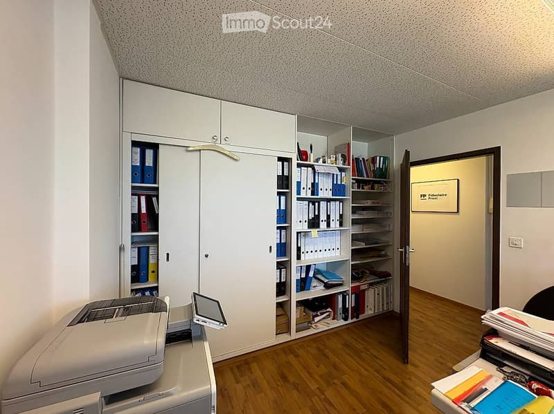 Office space with wooden flooring, white cabinet filled with folders and books, printer, and a screen on the desk.