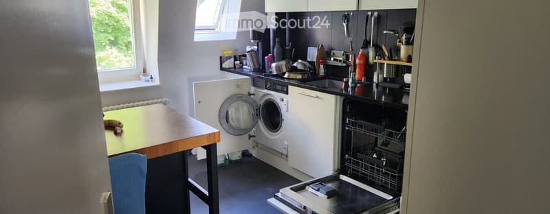 Modern kitchen with white cabinets, a dishwasher, a washing machine, a small table with a chair, and various kitchen items on the counter.