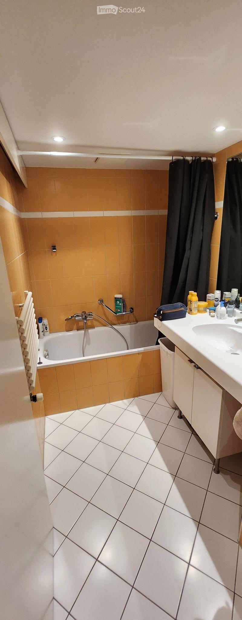 Bathroom with white tiled floor, bathtub, sink, and various toiletries on the counter. Orange tiles on the walls above the bathtub.