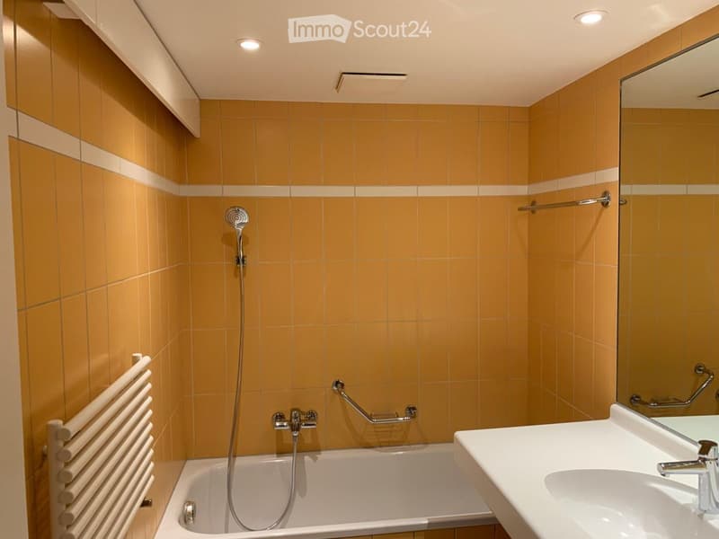 Modern bathroom with yellow tiles, a bathtub, a sink, a mirror, a showerhead, a towel rack, and a radiator.