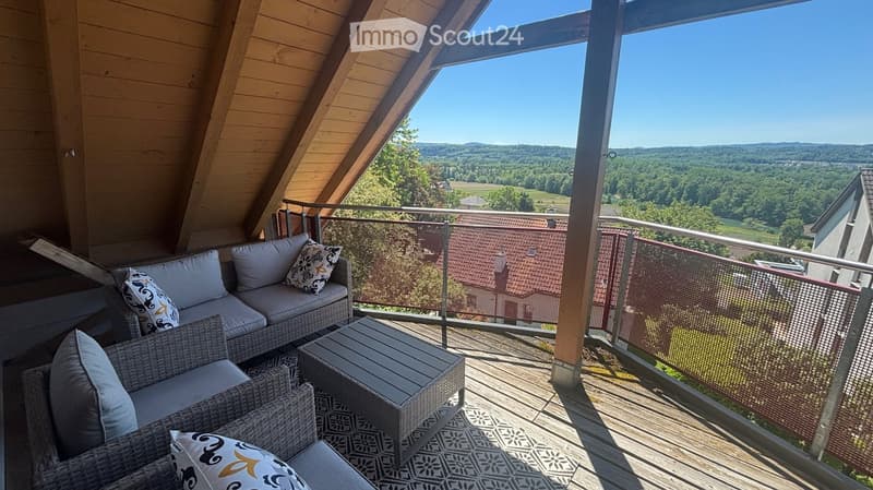 Wooden balcony with a scenic view, featuring a sofa, chairs, and a small table.