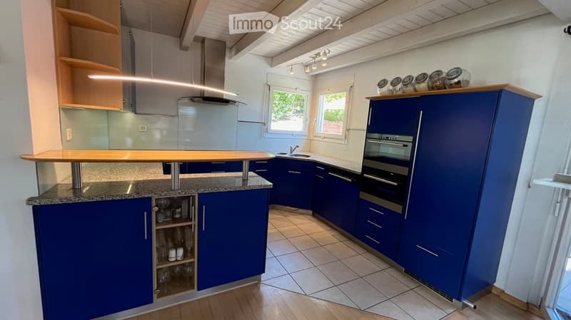 Modern kitchen with blue cabinets, granite countertop, built-in oven, and glassware on display.