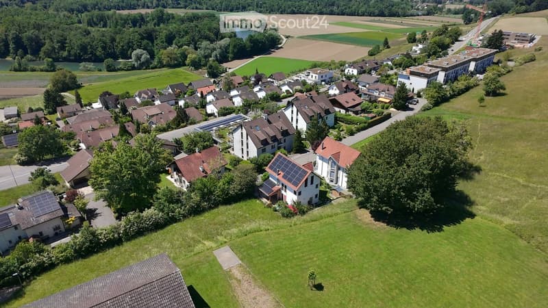 Aerial view of a residential neighborhood with multiple houses, green lawns, trees, and solar panels on some roofs.