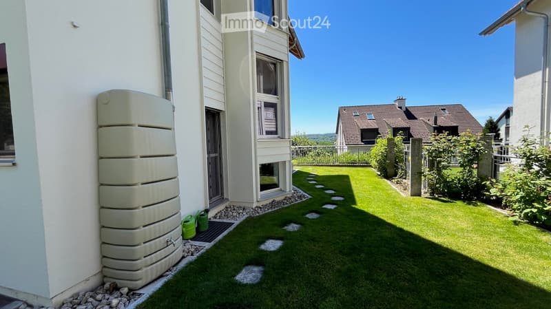 Well-maintained garden with green grass, stone pathway, and small water tank attached to the house.