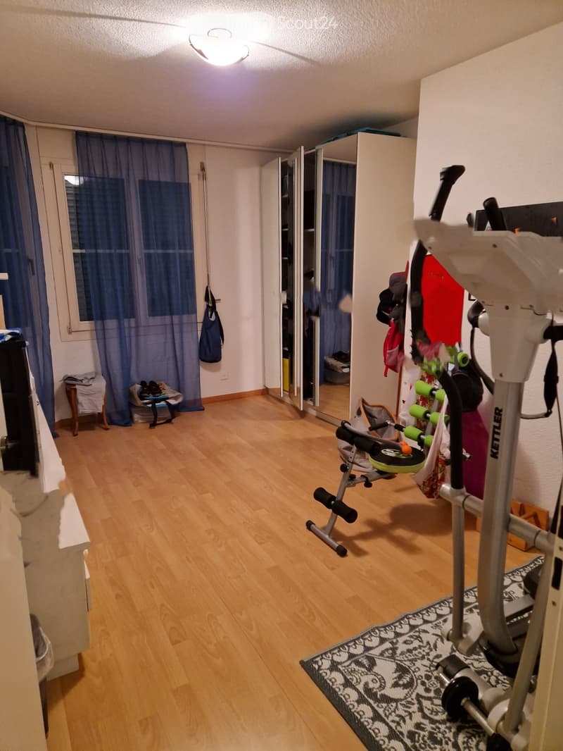 Exercise room with wooden flooring, exercise bike, mirror, small table, and chair.