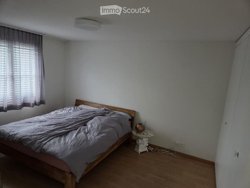 Bedroom with wooden bed, nightstand, table lamp, and window with blinds.