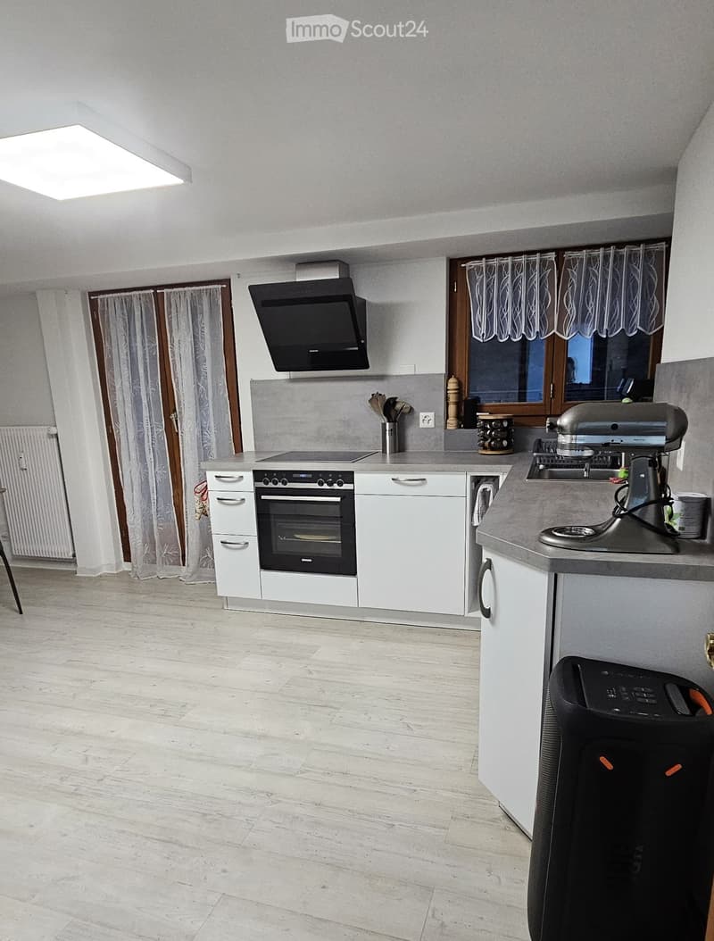 Modern kitchen with white cabinets, grey countertops, and a central island. Features an oven, range hood, mixer, and various kitchen appliances.