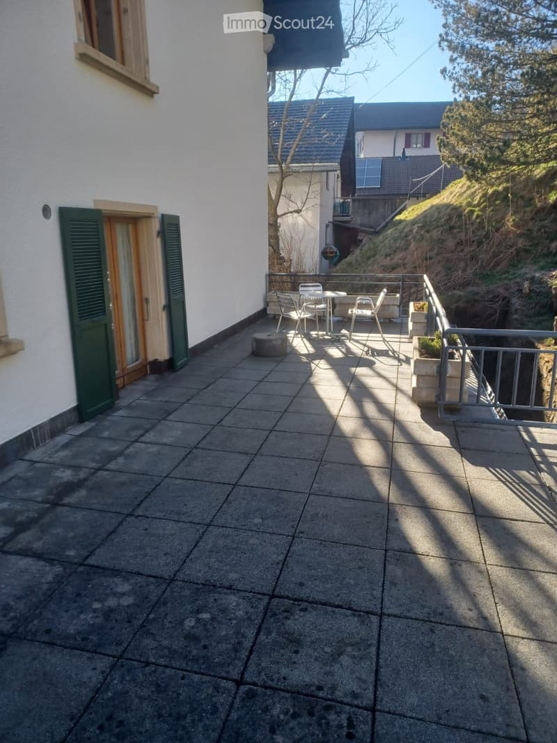 Balcony with tiled floor, metal railing, small table and chairs, and a view of the hillside.
