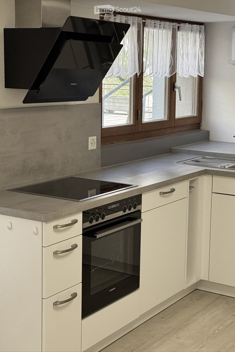 Modern kitchen with white cabinets, stainless steel appliances, and a large window with white curtains.