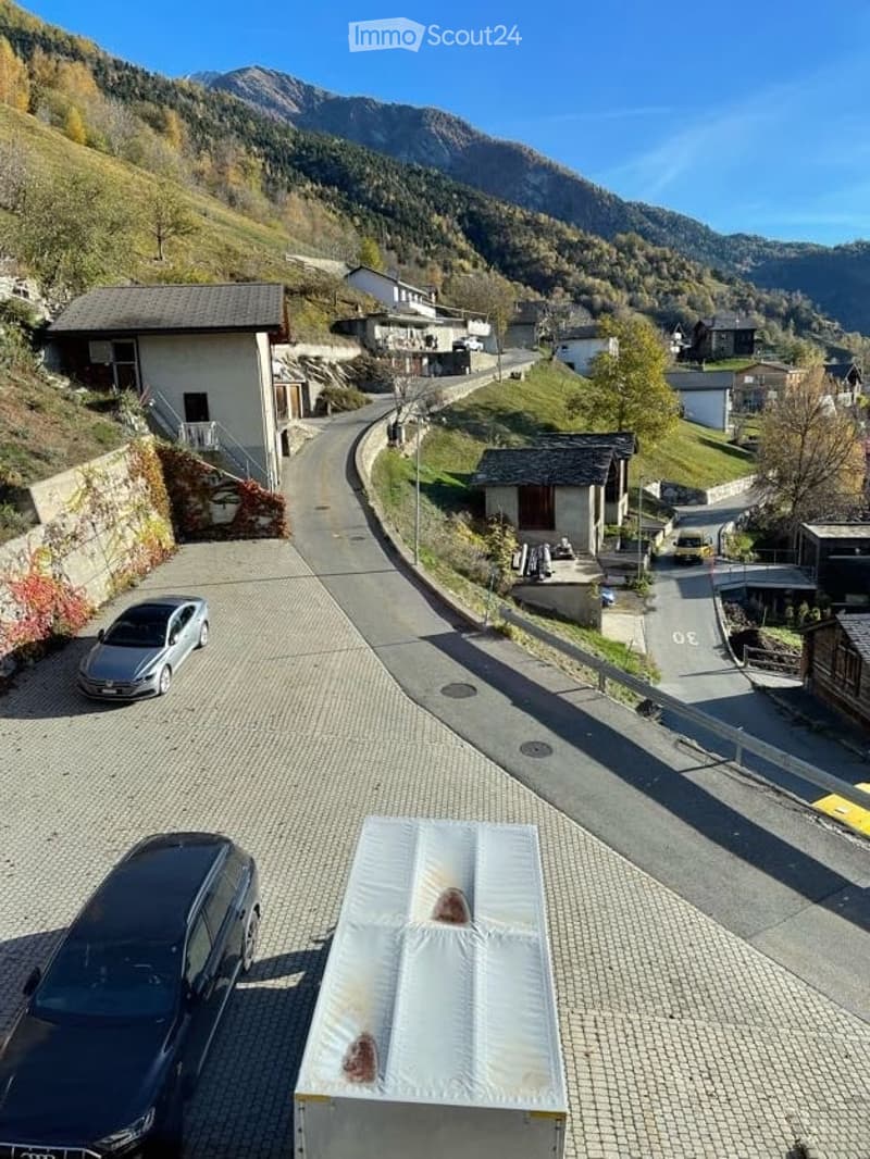 Aerial view of a residential area with parked cars, houses, and a scenic mountain backdrop.