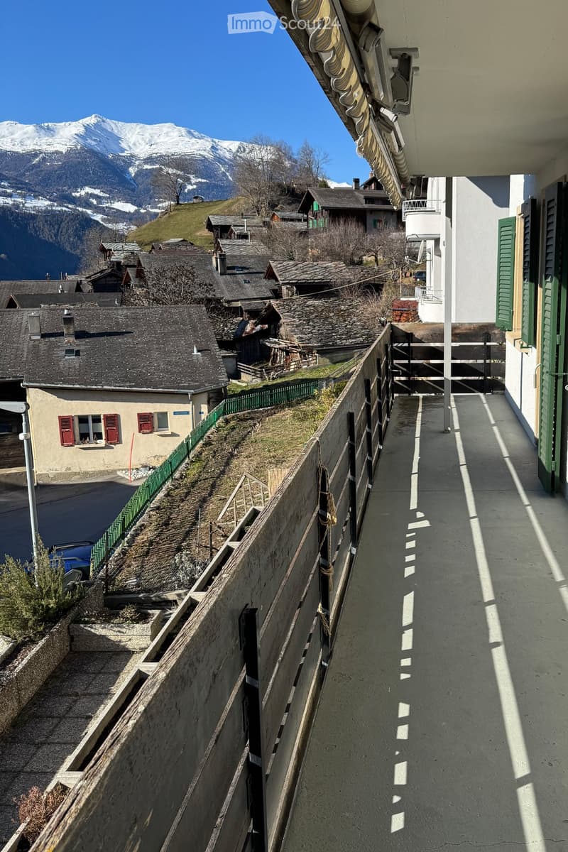 Balcony overlooking a village with traditional houses and a snow-capped mountain in the background.