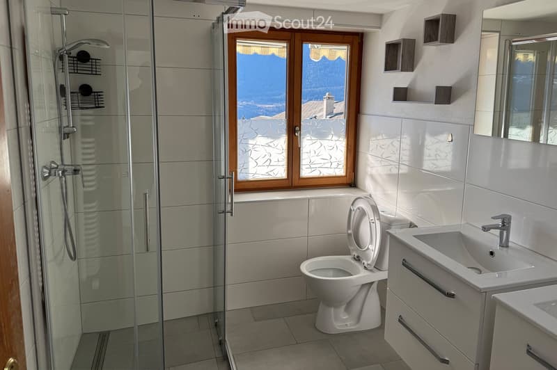 Modern bathroom with a glass-enclosed shower, toilet, sink, and a large window offering a scenic view.
