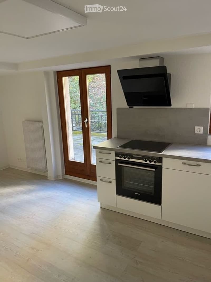 Modern kitchen with white cabinets, induction hob, oven, and a large window leading to a balcony.