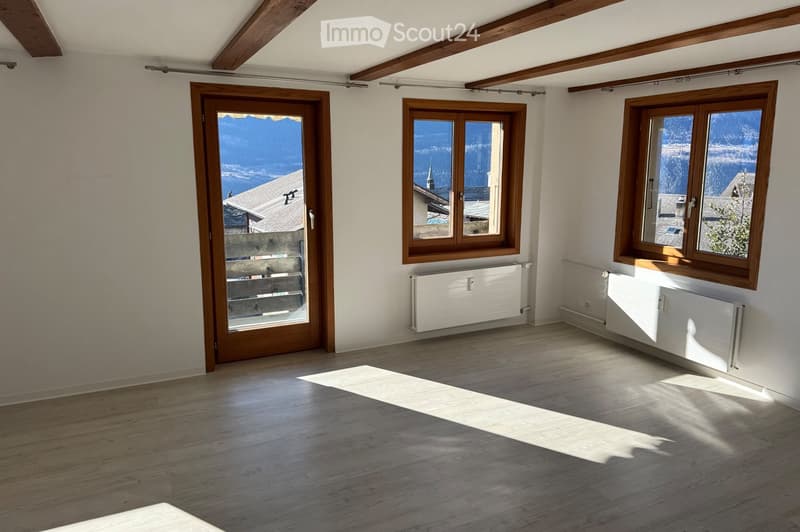Empty room with wooden flooring, white walls, large windows, and a sliding glass door leading to a balcony with a scenic mountain view.