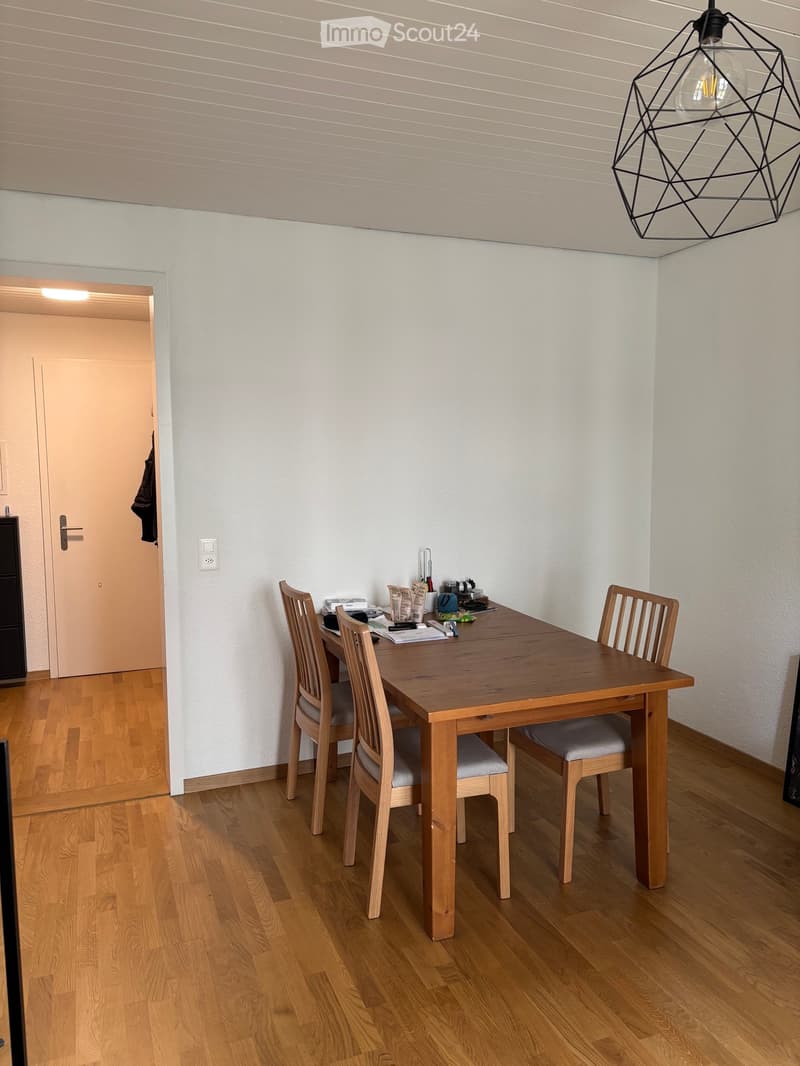 Dining room with wooden table, four chairs, and various items on the table, including cups and bottles. Light fixture hangs from the ceiling.