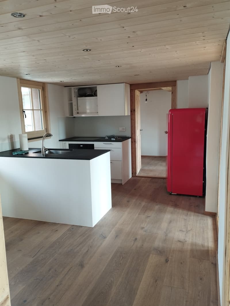 Modern kitchen with white cabinets, a red refrigerator, a black countertop, and a wooden floor.
