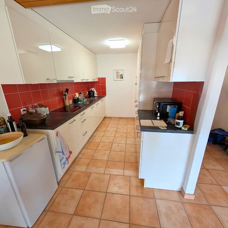 Modern kitchen with white cabinets, red tiled backsplash, and tiled floor. Features a refrigerator, microwave, oven, countertop, and various kitchen items.