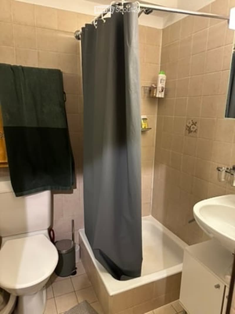 Bathroom with a toilet, bathtub, shower curtain, sink, towel, and trash can.
