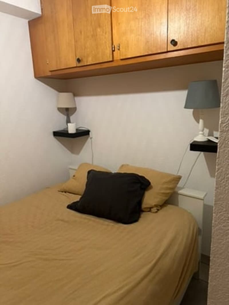 Cozy bedroom with a single bed, pillows, nightstands, lamps, and wooden cabinets.