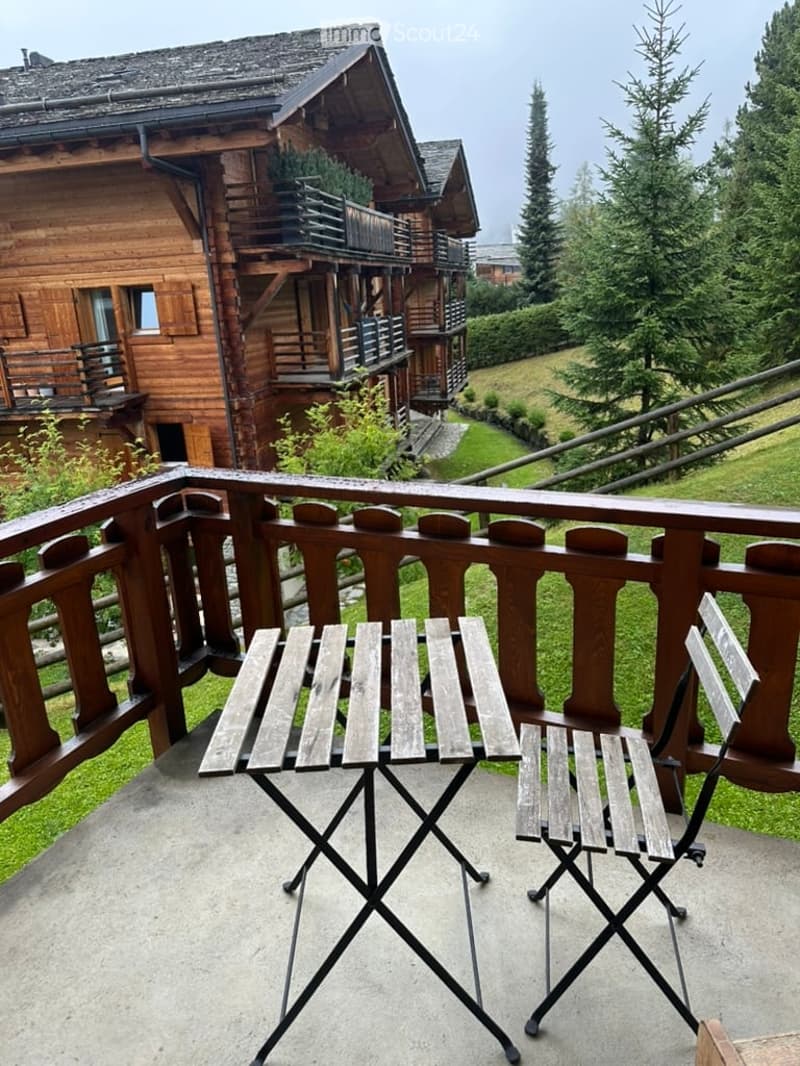 Balcony with wooden railing, concrete floor, and a small table with two chairs.