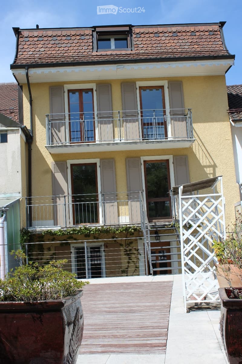 Two-story residential building with a balcony, wooden deck, and stairs leading to the entrance.