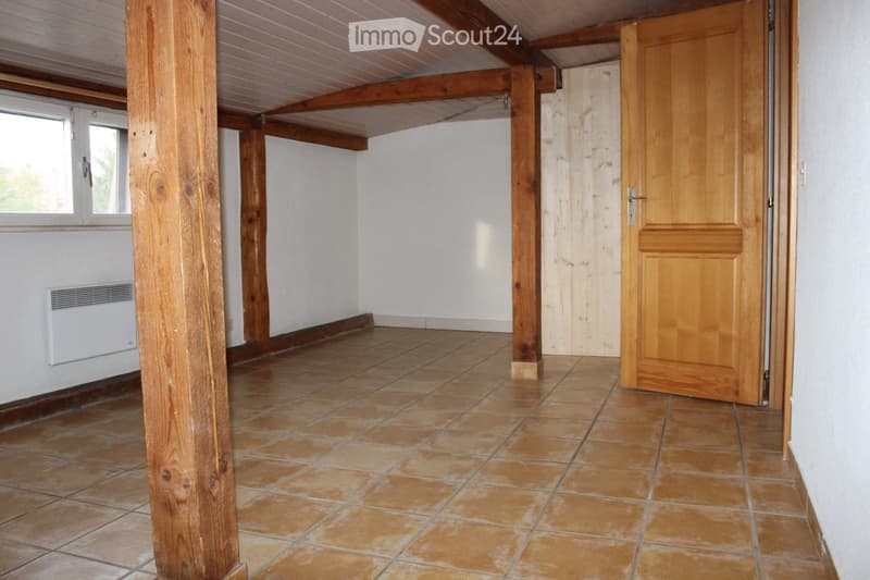 Empty room with exposed wooden beams, tiled floor, and a single wooden door.