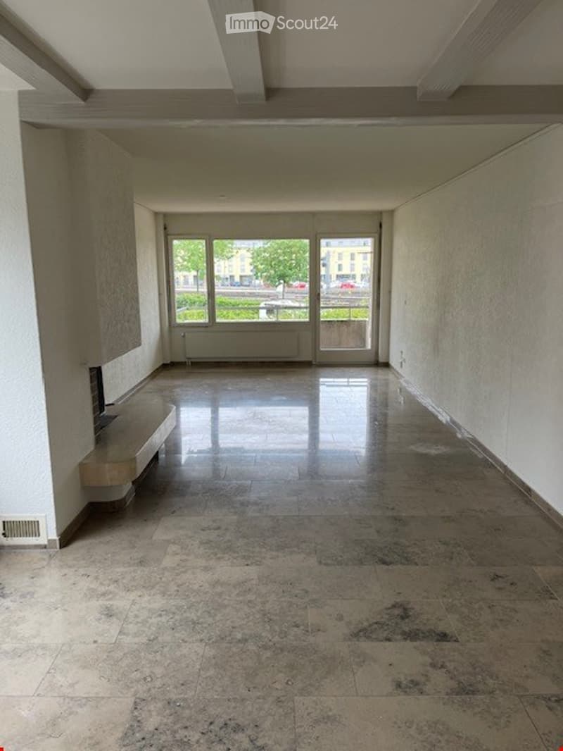 Empty hallway with large windows at the far end, polished tile floor, and a small bench against the left wall.
