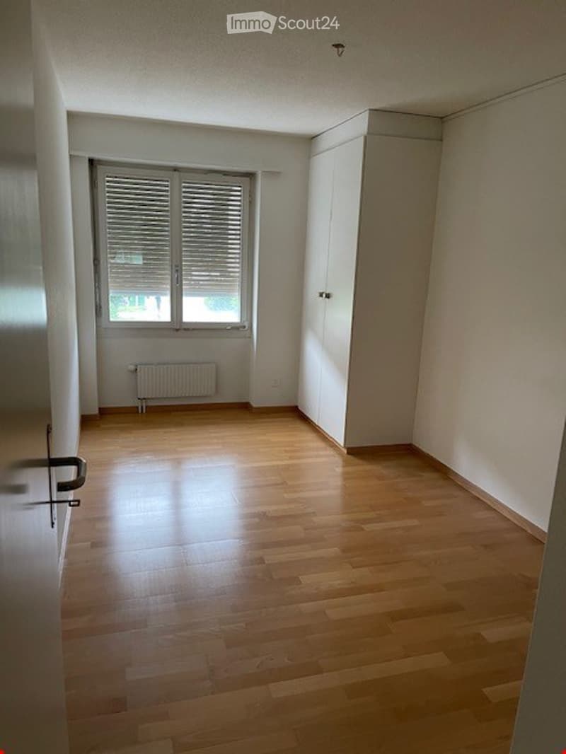 Empty room with wooden flooring, white walls, a window with blinds, and a built-in closet.